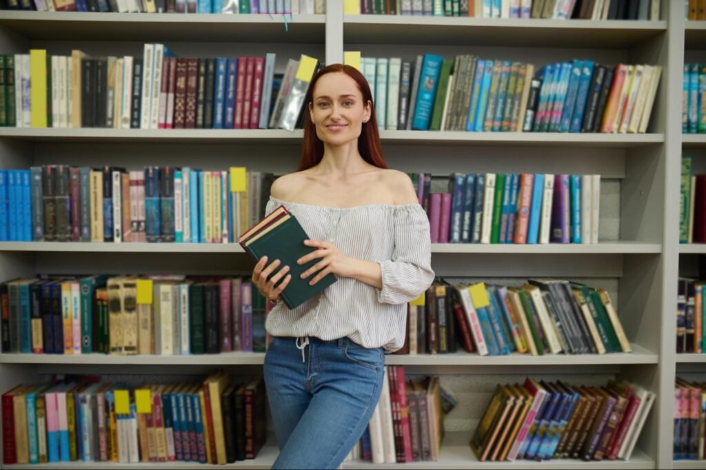 A smiling author holding books in front of a bookshelf, representing successful book publishing and distribution.